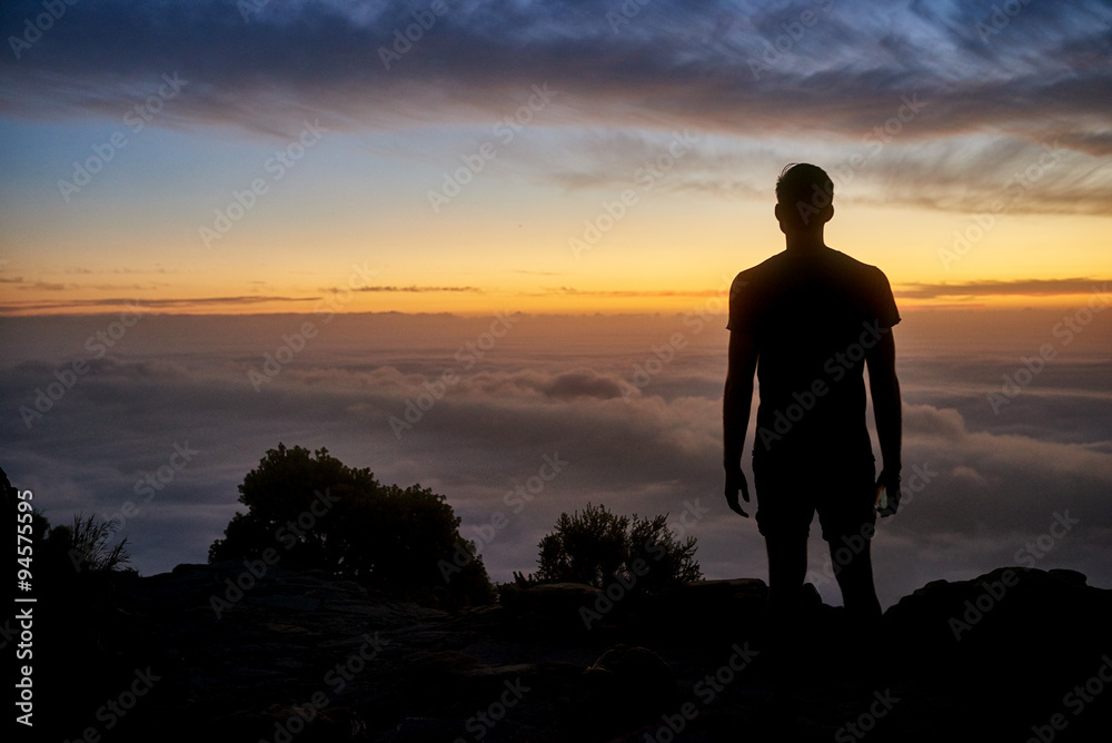 Silhouette of a man on a mountain with a  cloudy sunrise