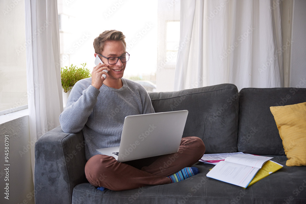 © marvent - Guy smiling while on the phone at home with his laptop