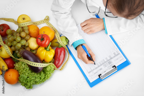 Doctor therapist writing case development form sitting at the desk in hospital. Female nutritionist prescribing diet to patient. 