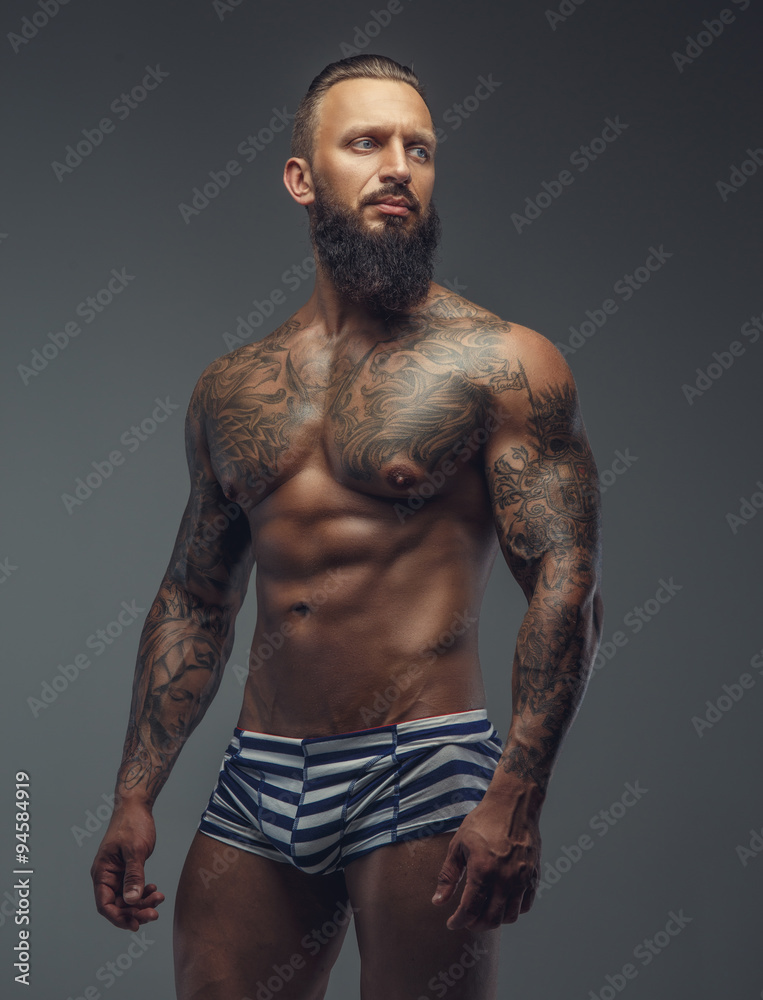 Tattooed muscular man with beard in stripes panties. Tattooed muscular man with beard in stripes panties.