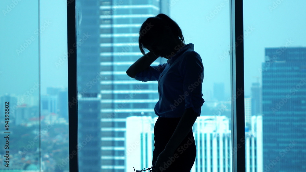 Tired businesswoman having neck pain standing by window in office
