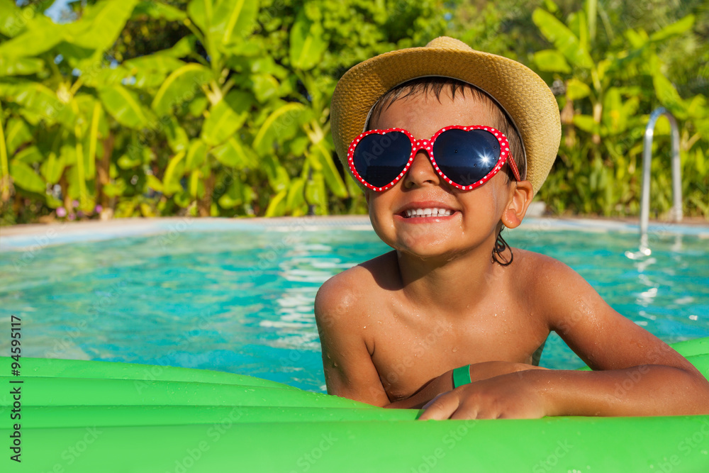 Boy in heart-shaped sunglasses on green airbed