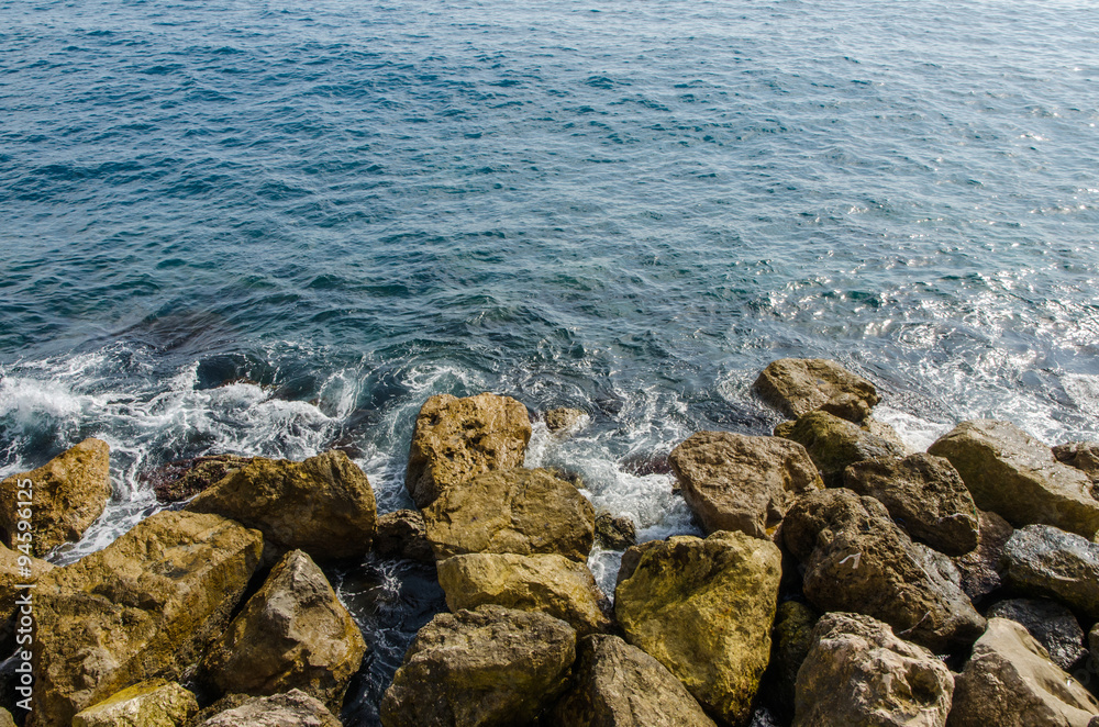 top view of waves of the mediterranean sea water crushing into reddish rocks of the shore top view of waves of the mediterranean sea water crushing into reddish rocks of the shore