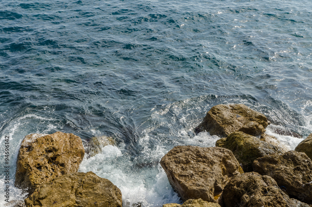 close-up of waves of the mediterranean sea water crushing into reddish rocks of the shore on a sunny day close-up of waves of the mediterranean sea water crushing into reddish rocks of the shore on a sunny day