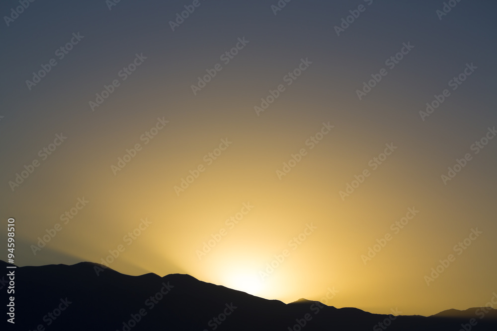 Dramatic sunset rays behind silhouette of of mountain Dramatic sunset rays behind silhouette of of mountain