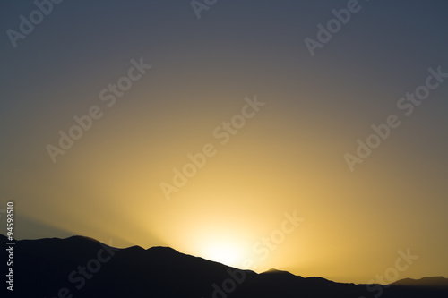 Dramatic sunset rays behind silhouette of of mountain