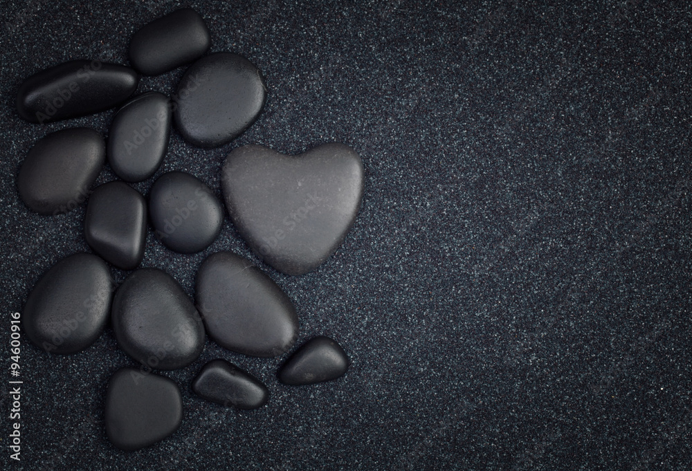 Black stones with black zen heart shaped rock on grain sand