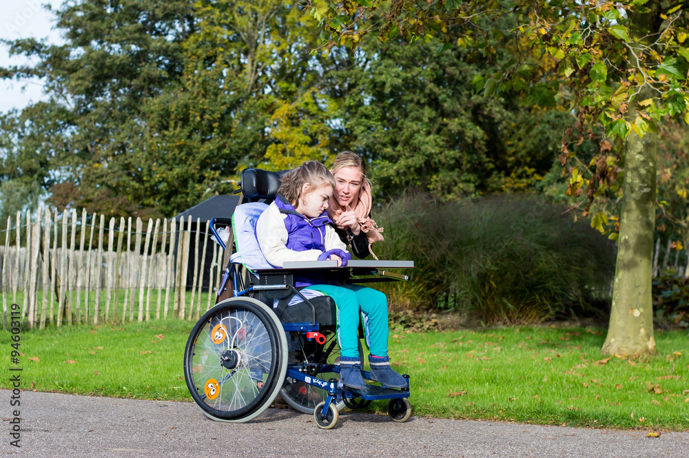 Disability/ A disabled child in a wheelchair with a carer outside Disability/ A disabled child in a wheelchair with a carer outside