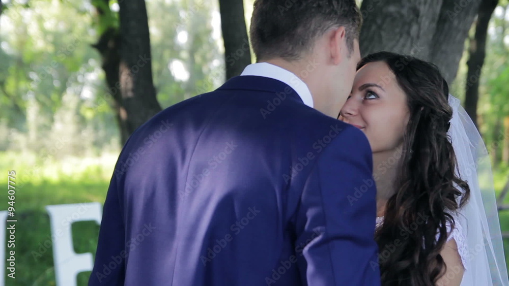bride and groom embracing tenderly kissing in a green park smile and happiness on his face bride and groom embracing tenderly kissing in a green park smile and happiness on his face