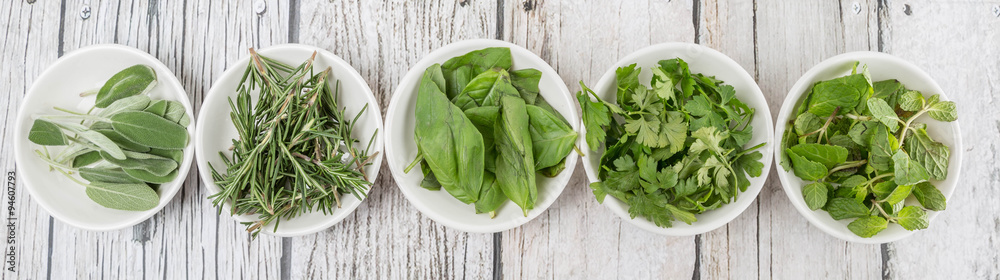 Basil leaves, rosemary. mint, parsley and sage leaves herbs in white bowl over wooden background Basil leaves, rosemary. mint, parsley and sage leaves herbs in white bowl over wooden background