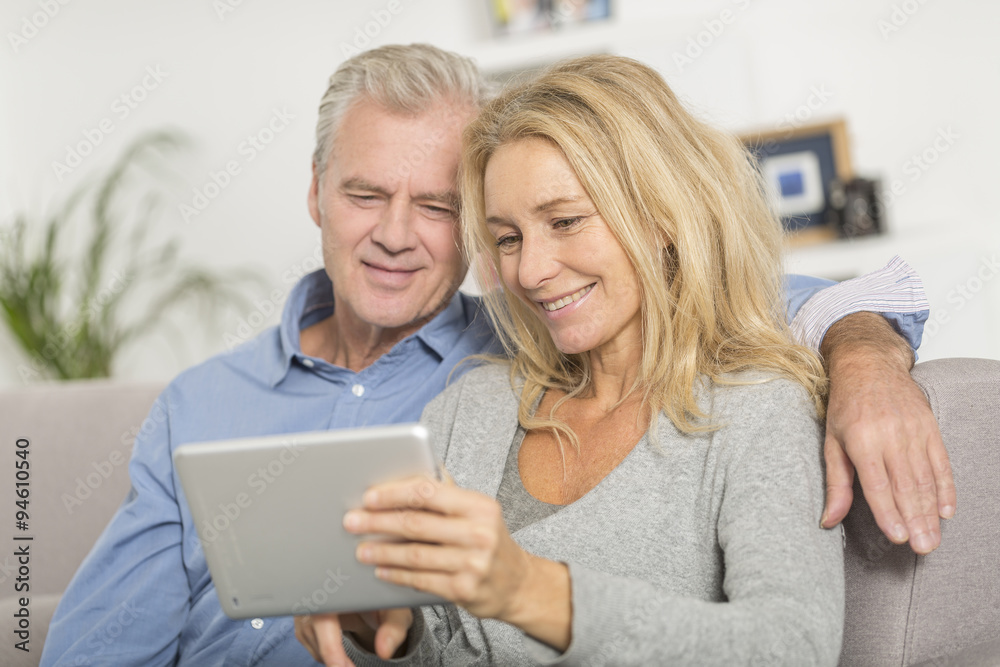 Mature couple sitting in sofa and using tablet pc Mature couple sitting in sofa and using tablet pc