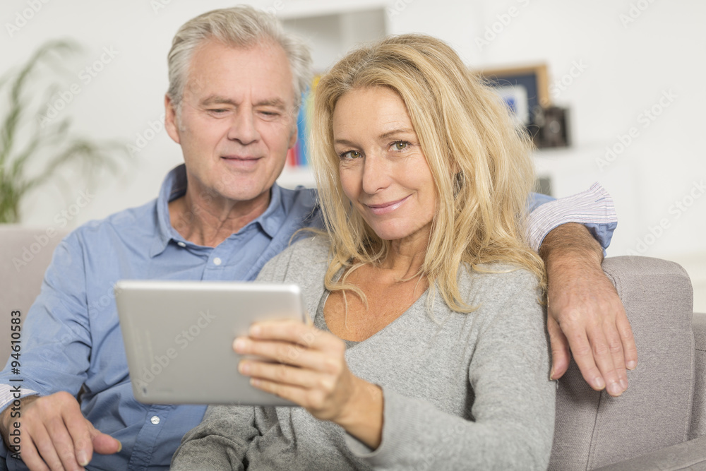 Mature couple sitting in sofa and using tablet pc Mature couple sitting in sofa and using tablet pc