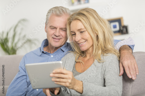 Mature couple sitting in sofa and using tablet pc