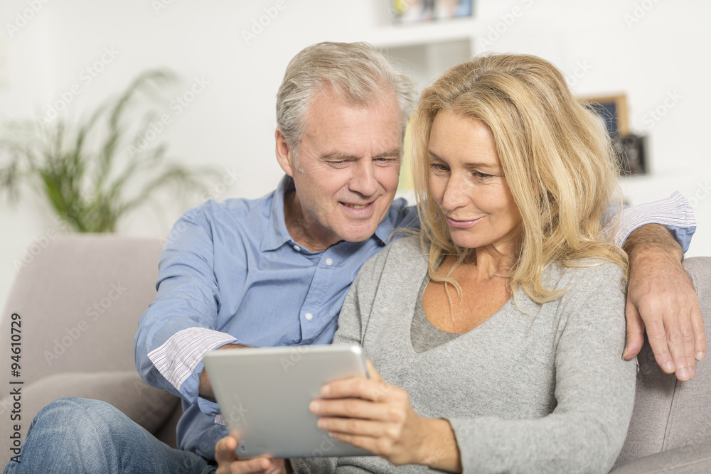 Mature couple sitting in sofa and using tablet pc Mature couple sitting in sofa and using tablet pc