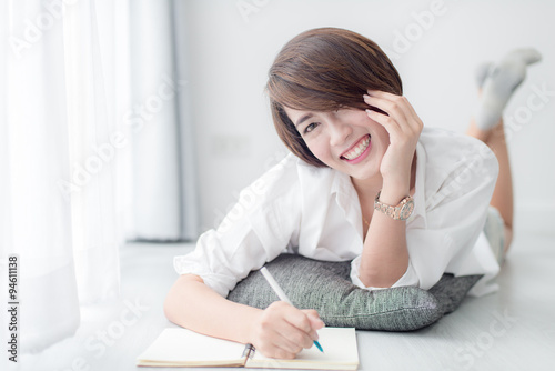 Happy Asian woman lying down on floor and writting at home.