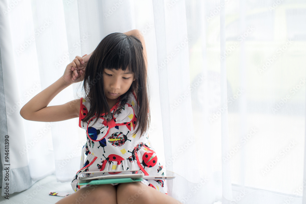 Asian girl playing with her tablet pc or tab in her house sittin Asian girl playing with her tablet pc or tab in her house sittin