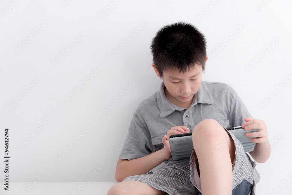 Boy using digital tablet while sitting with white wall. Boy using digital tablet while sitting with white wall.
