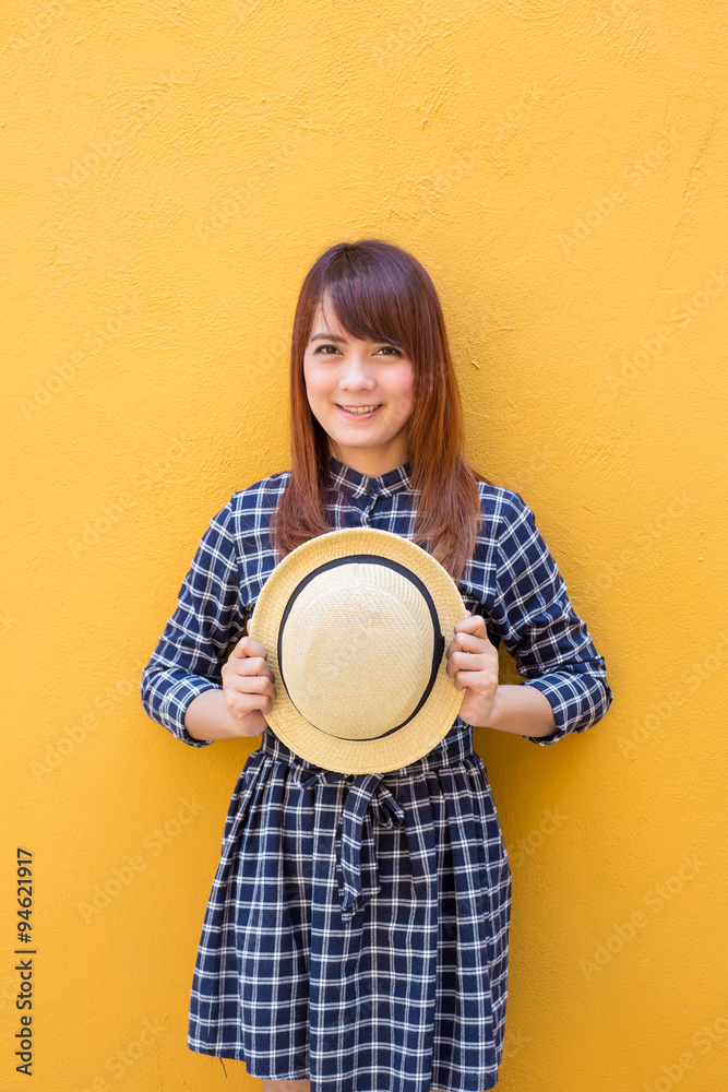 smiling woman wear in dress hand holding hat on yellow cement wall background smiling woman wear in dress hand holding hat on yellow cement wall background
