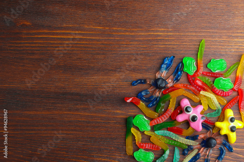 colorful jelly candies in the shape of a worm and spider on a brown wooden background