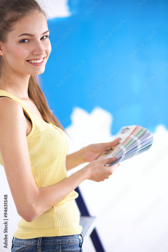 Happy beautiful young woman doing wall painting, standing near ladder Happy beautiful young woman doing wall painting, standing near ladder