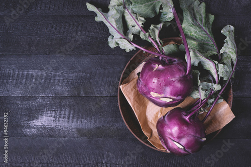 Kohlrabi cabbage with green leaves on a metal plate on a black wooden background top view