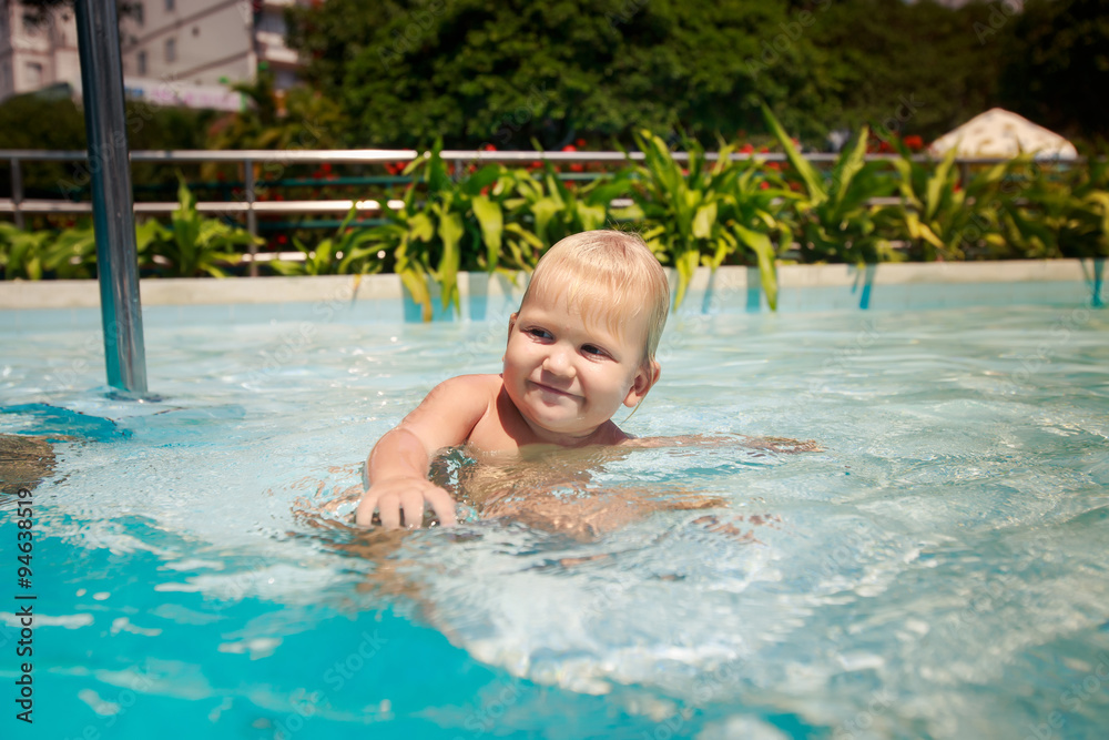 small blonde girl bathes smiles in hotel swimming pool