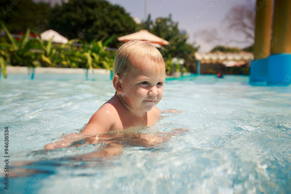 small blonde girl bathes smiles plays in hotel swimming pool
