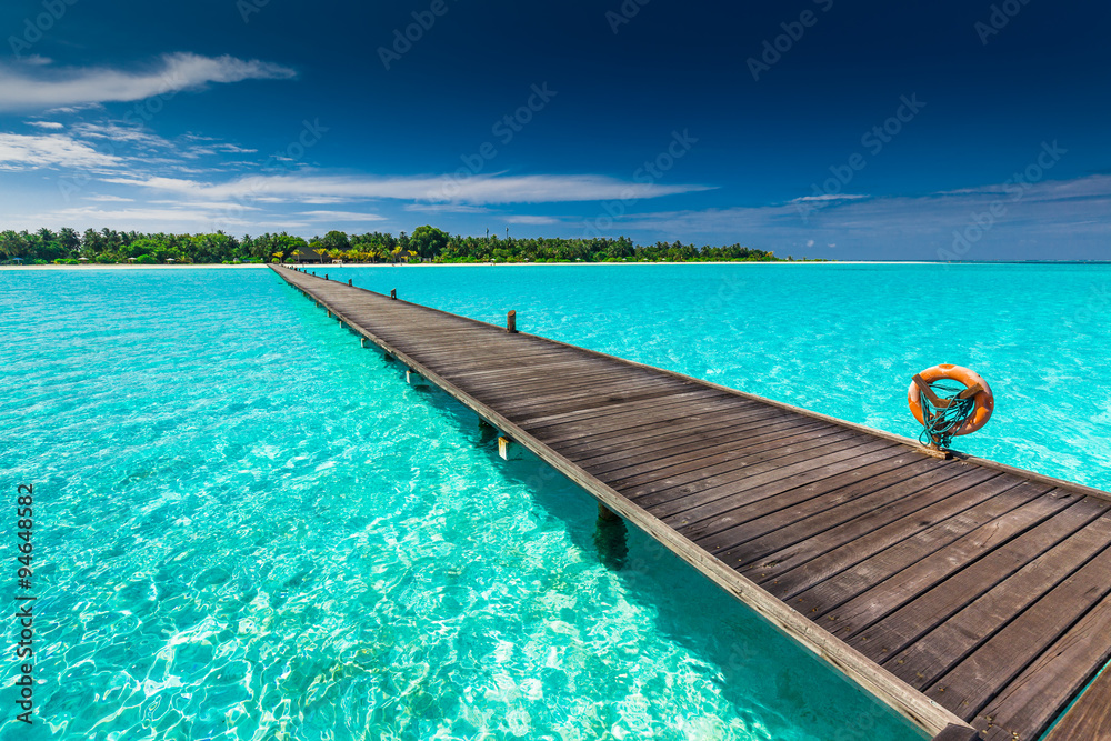 Naklejka premium Długi drewniany pomost nad atolem i tropikalna wyspa na Malediwach