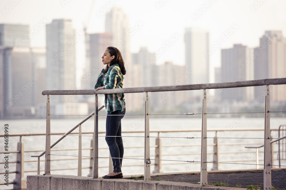 A woman standing on the waterfront, view to the city over the water in New York City. 