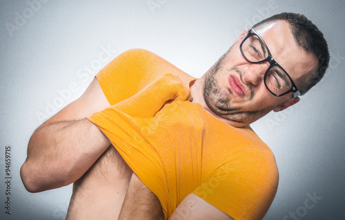 Funny young man get undressing. T-shirt is  closely or narrowly. Nervous guy isolated on gray background.