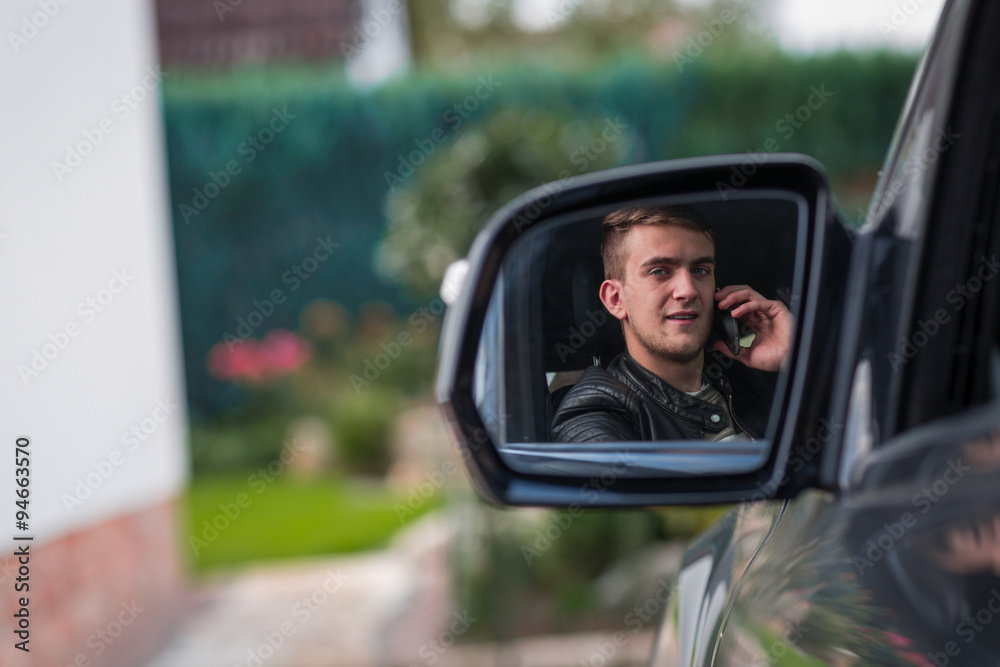 portrait of young adult behind steering wheel inside a car making a phone call with his smartphone