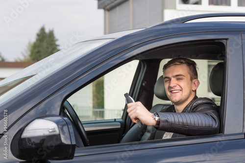Happy young man smiling in new car holding car keys 