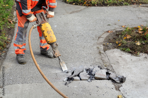 Worker at construction site demolishing asphalt with pneumatic plugger hammer