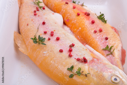 golden trout on a baking dish with red pepper and thyme. gold fish. home kitchen.