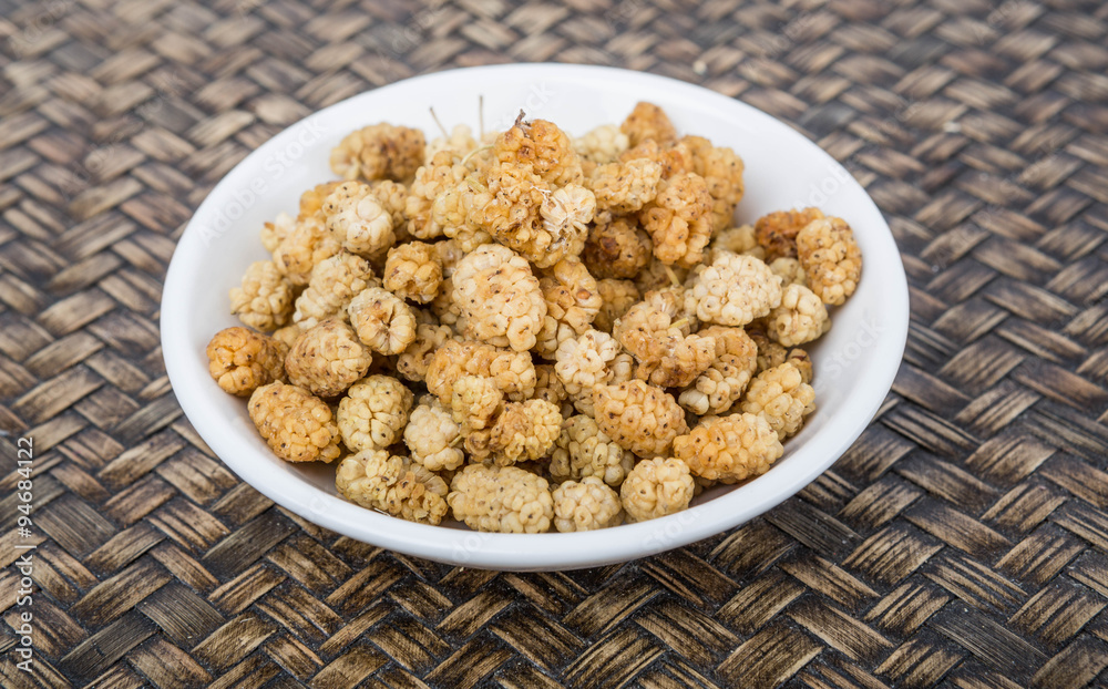 Dried white mulberry in a white bowl over wicker background