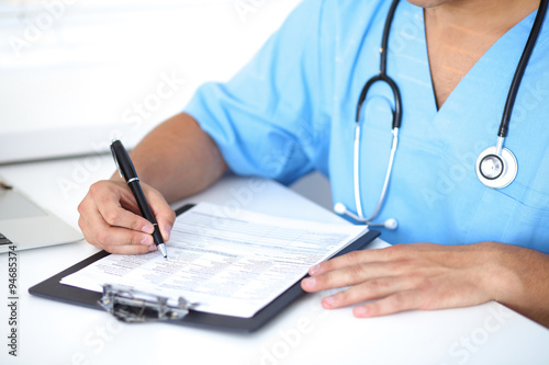 Portrait of unknown male surgeon doctor holding his stethoscope and filling up medical prescription