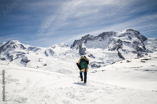 A man in camouflage winter coat and backpack standing in front of the background of snow mountain.