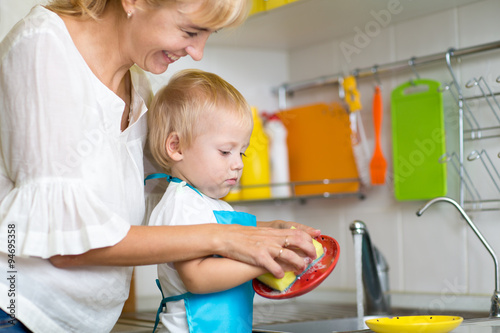 Fotografie Kid boy and mother washing dishes - having fun together in the kitchen
