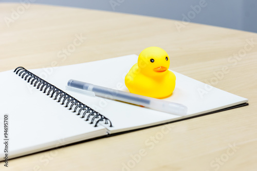 Pen and notebook and Rubber Duck on wooden desk