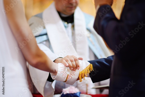 Bride and groom's hands wrapped in priest's cassock photo