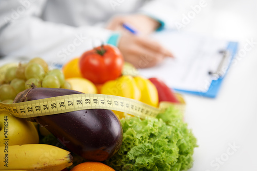 Healthy nutrition concept. Close-up of fresh vegetables and fruits with measuring tape lying on doctor's desk. 