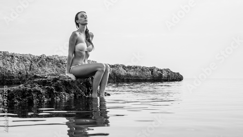 Beautiful young woman portrait sit on the rocks on the beach. 