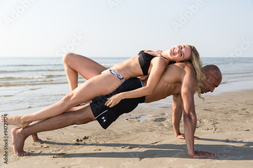Woman lying on a man doing push-ups at beach