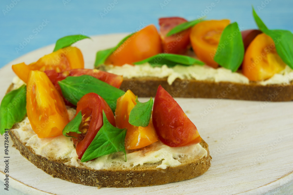 Bruschetta with soft cheese, basil and cherry tomatoes on a wood