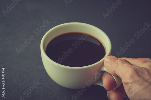 Male hand holding cup of black coffee, vintage image