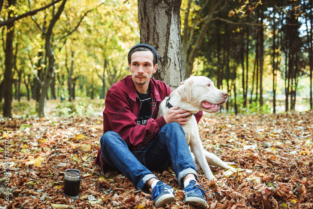 Fototapeta premium man drinking coffee in park and playing with labrador dog
