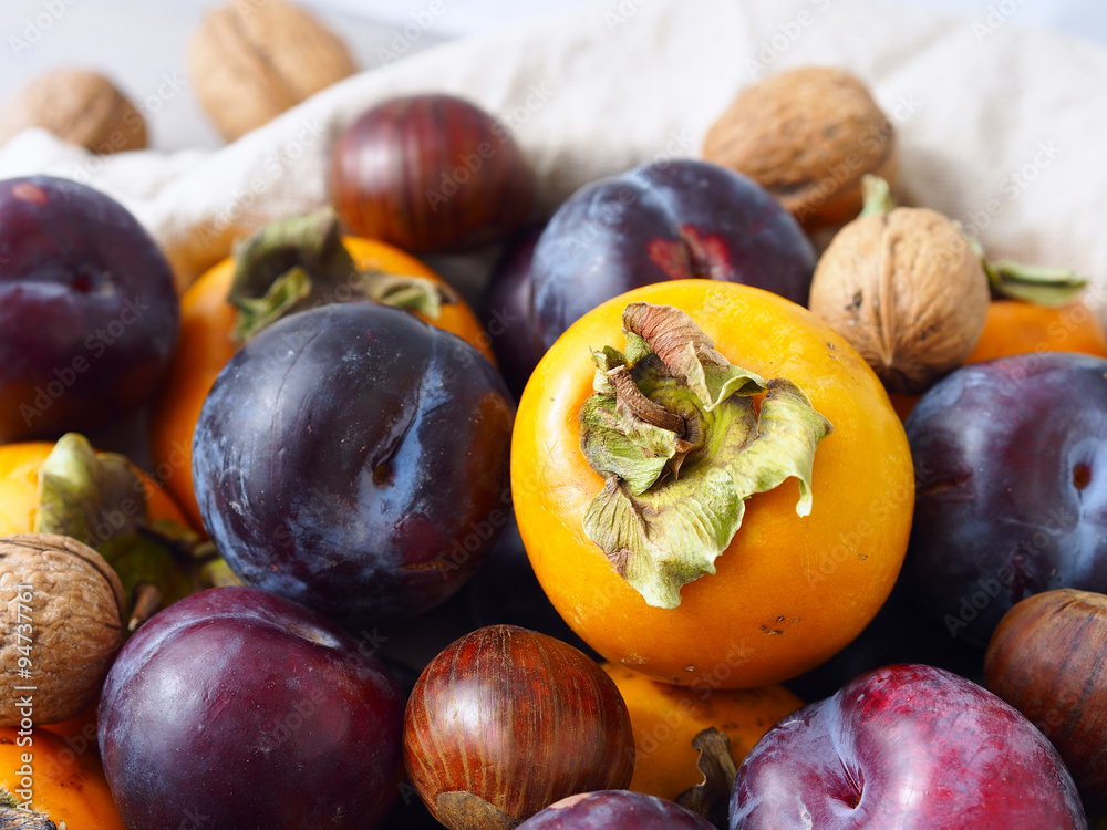Fototapeta premium Persimmons with purple plums, chestnuts and walnuts. Fall still life
