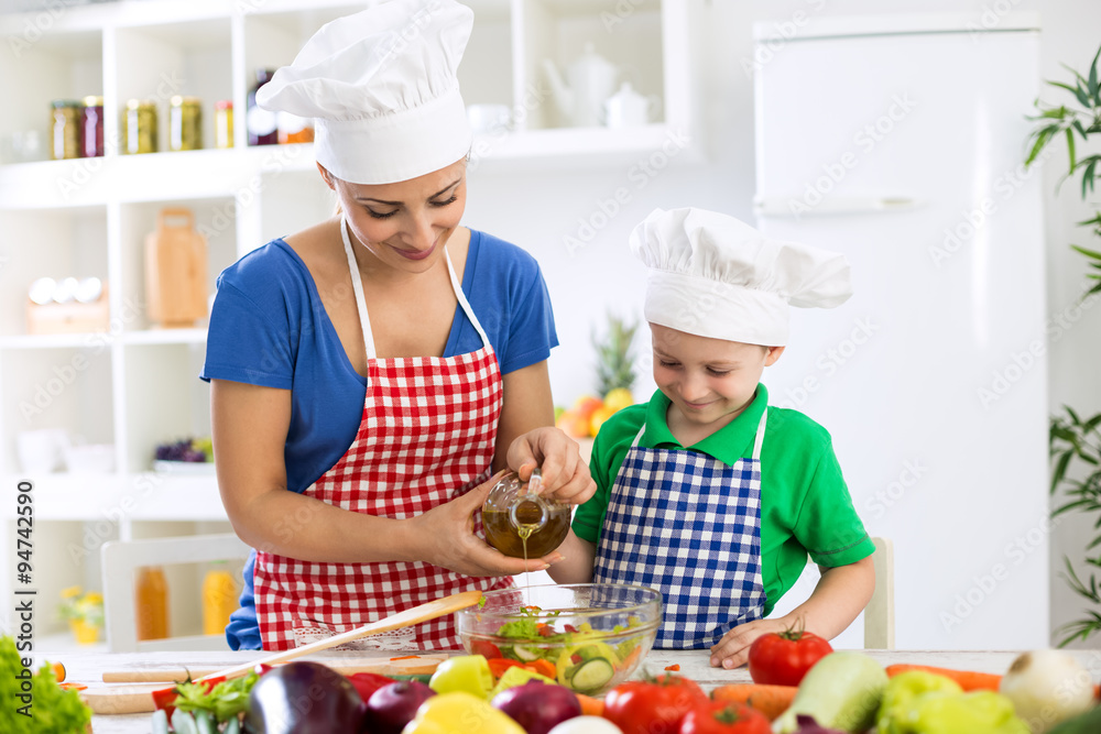 Mother and child putting olive oil to vegetables lettuce Mother and child putting olive oil to vegetables lettuce