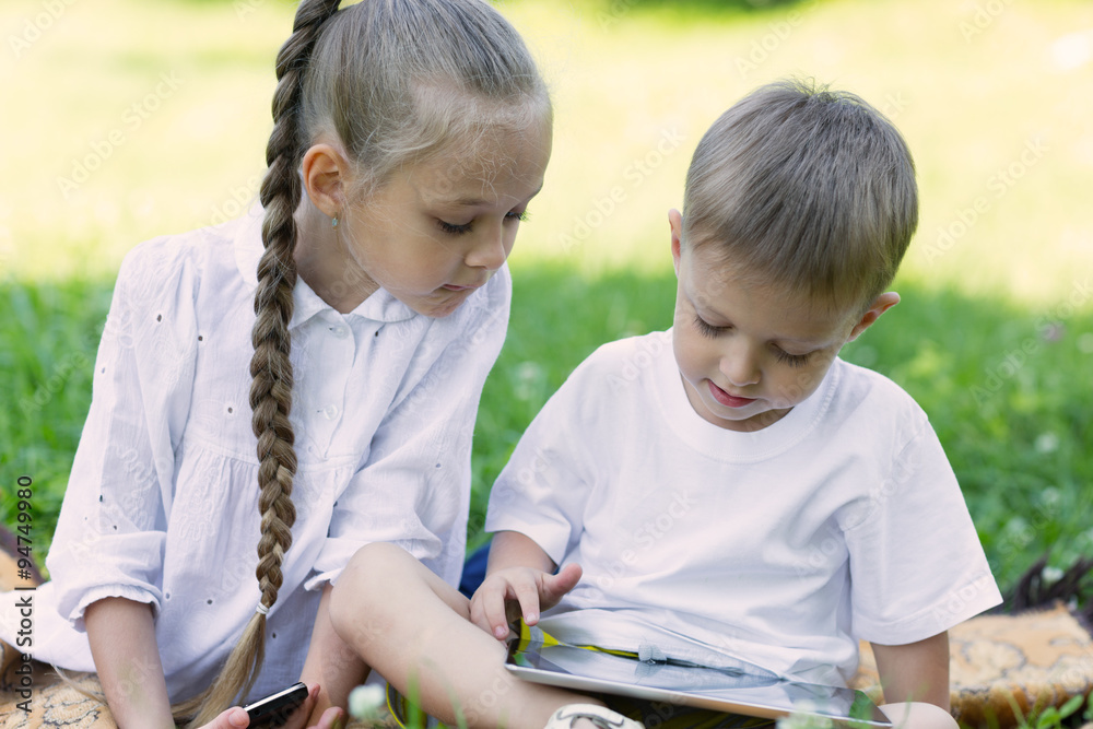 Happy kids using tablet PC on the grass