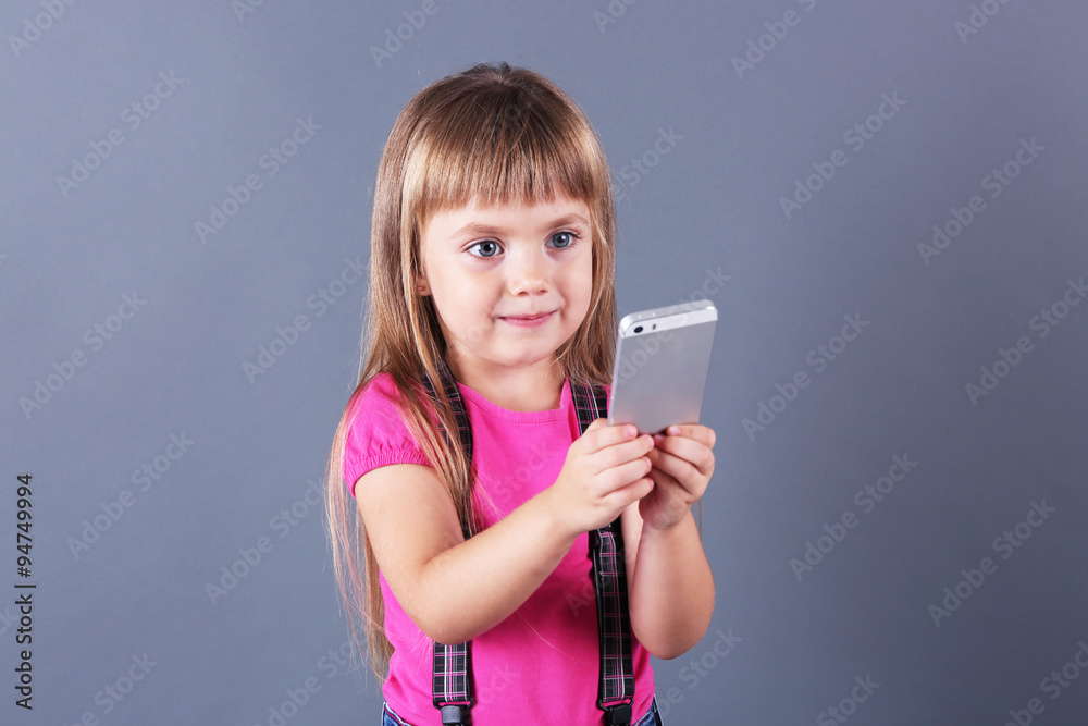 Beautiful little girl with mobile phone, on grey background Beautiful little girl with mobile phone, on grey background
